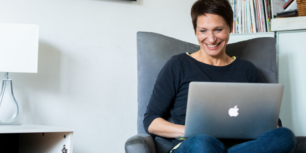 Texterin Inga Symann sitzt entspannt im Sessel, hat ihren Laptop auf dem Schoß und schreibt Texte.